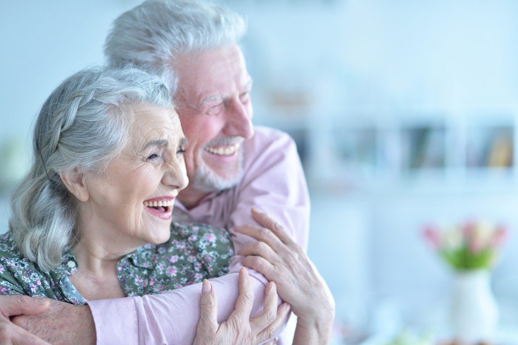 An older couple smiling and hugging, looking off into the distance.