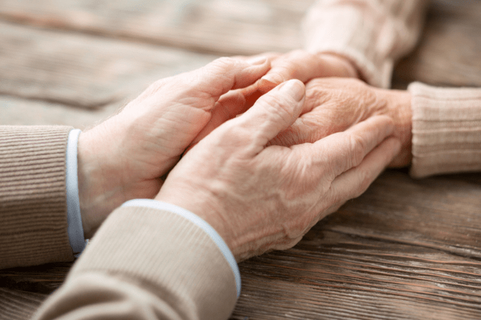 Close-up of elderly hands gently holding each other on a wooden table, symbolizing care and support.