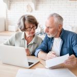 Busy caucasian old elderly senior couple making calculations at home kitchen, checking the document, revising data, information, counting domestic bills and rentals