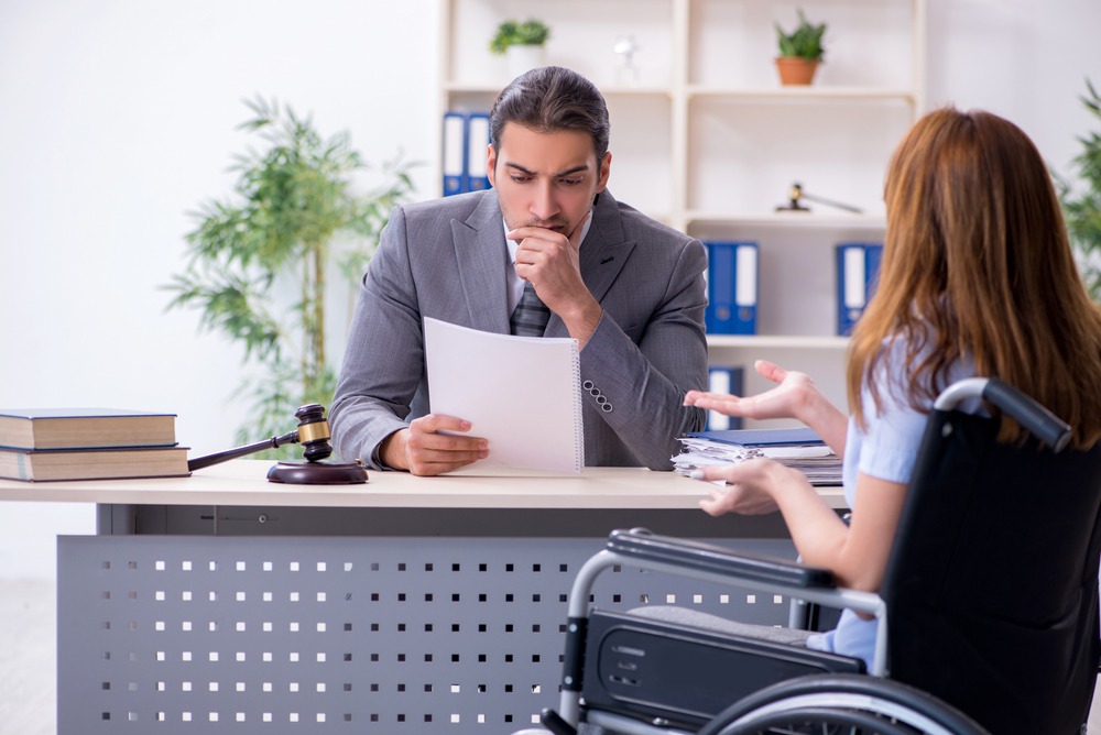 Attorney reviewing disability case documents with client in wheelchair