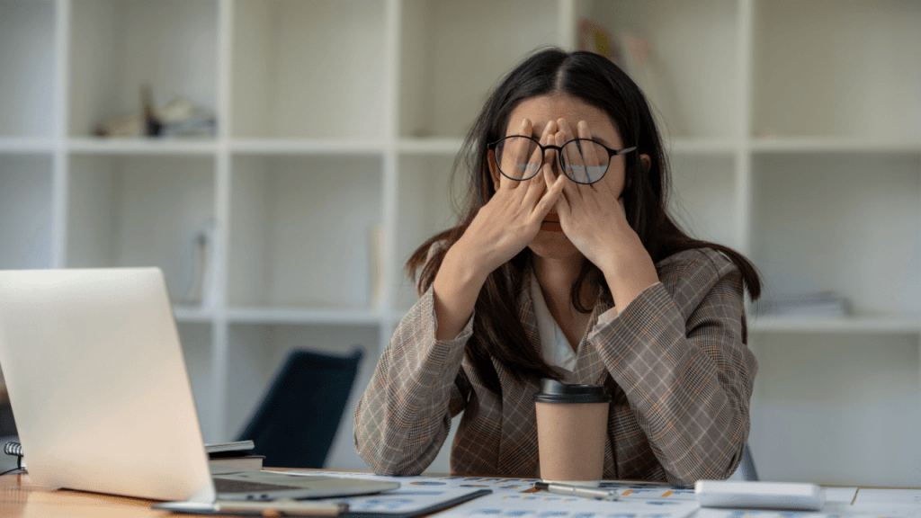 Can you get SSDI for depression Stressed businesswoman rubbing her eyes while working at desk with laptop and paperwork in modern office