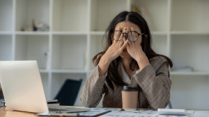 Can you get SSDI for depression Stressed businesswoman rubbing her eyes while working at desk with laptop and paperwork in modern office