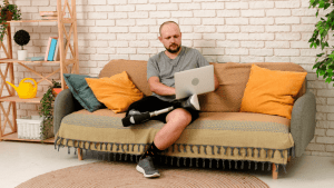 How are SSDI benefits determined Man with prosthetic leg working on laptop while sitting on couch in modern living room with plants and decorative elements
