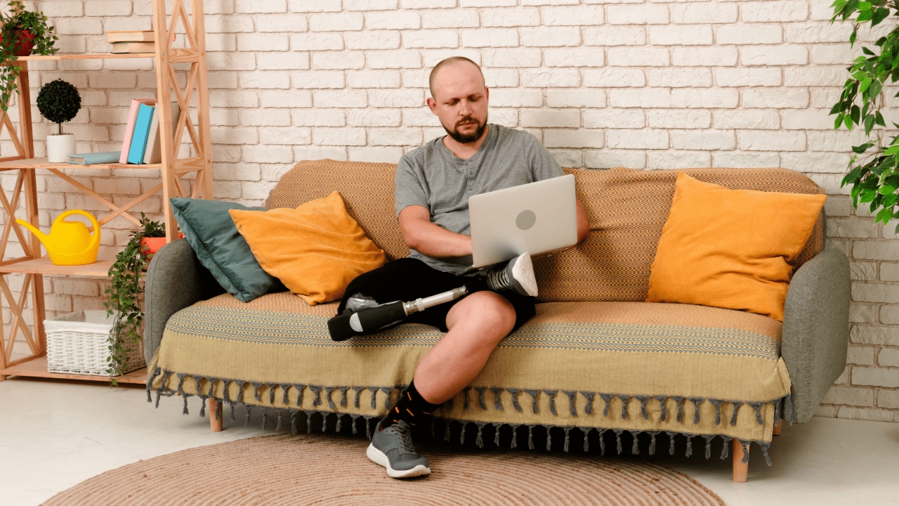 How are SSDI benefits determined Man with prosthetic leg working on laptop while sitting on couch in modern living room with plants and decorative elements