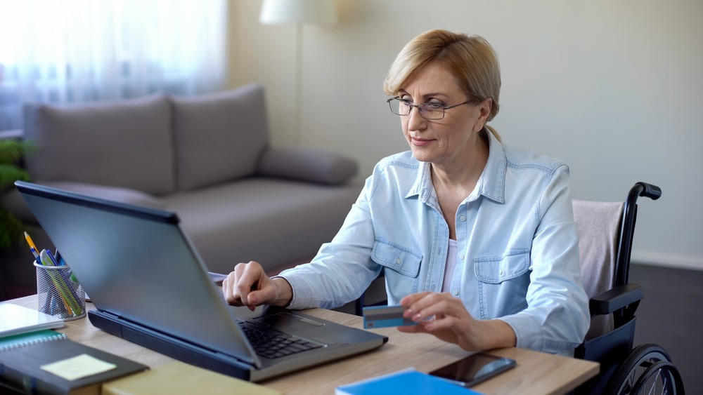Woman in wheelchair using laptop and holding credit card