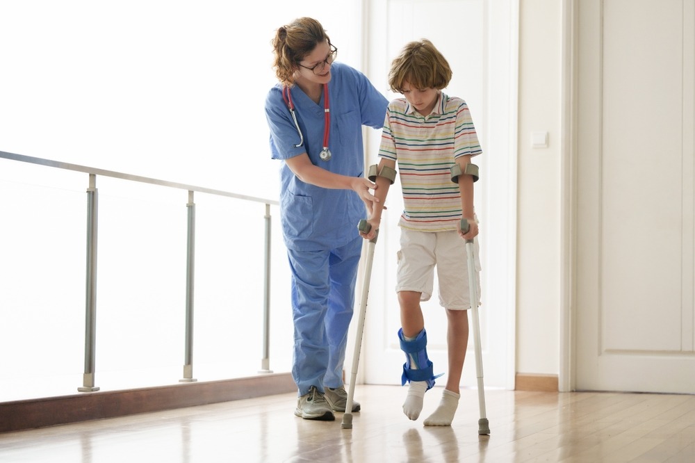 Nurse assisting a young boy on crutches with a leg brace