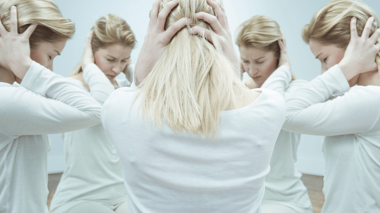 Woman experiencing mental distress surrounded by multiple reflections of herself in white clothing against light background
