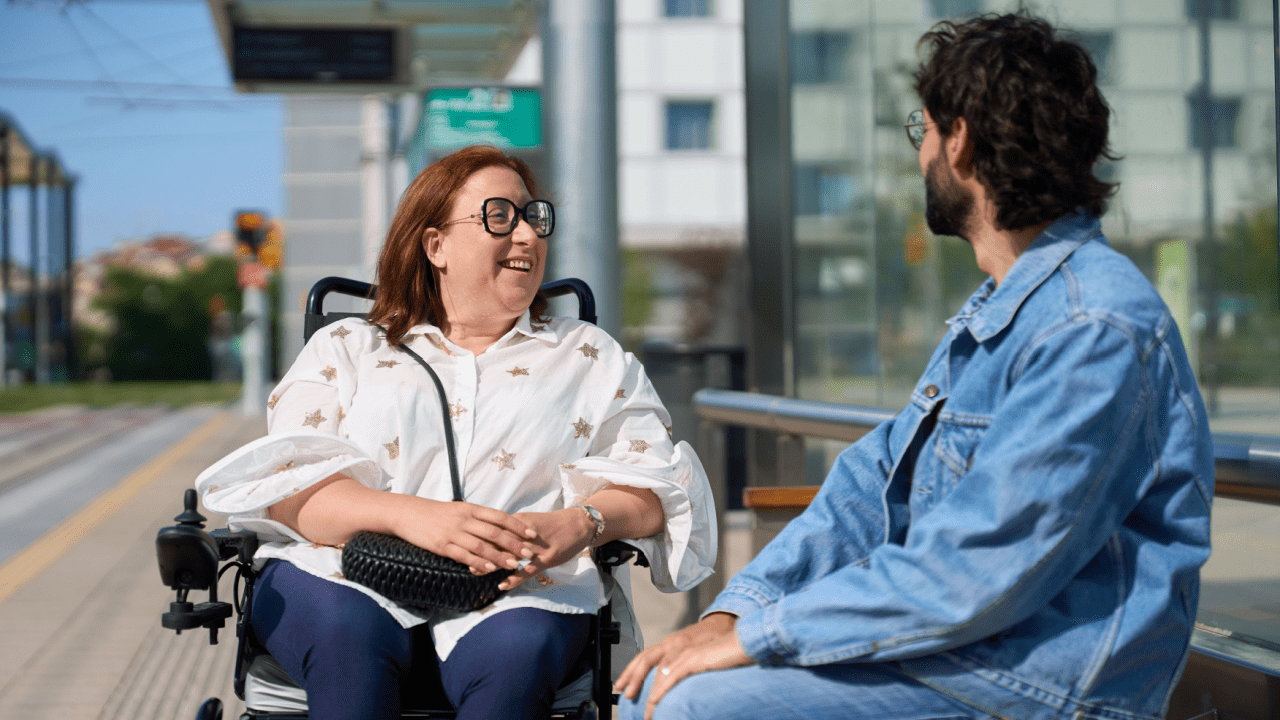 Woman in wheelchair having friendly conversation with man at public transit station