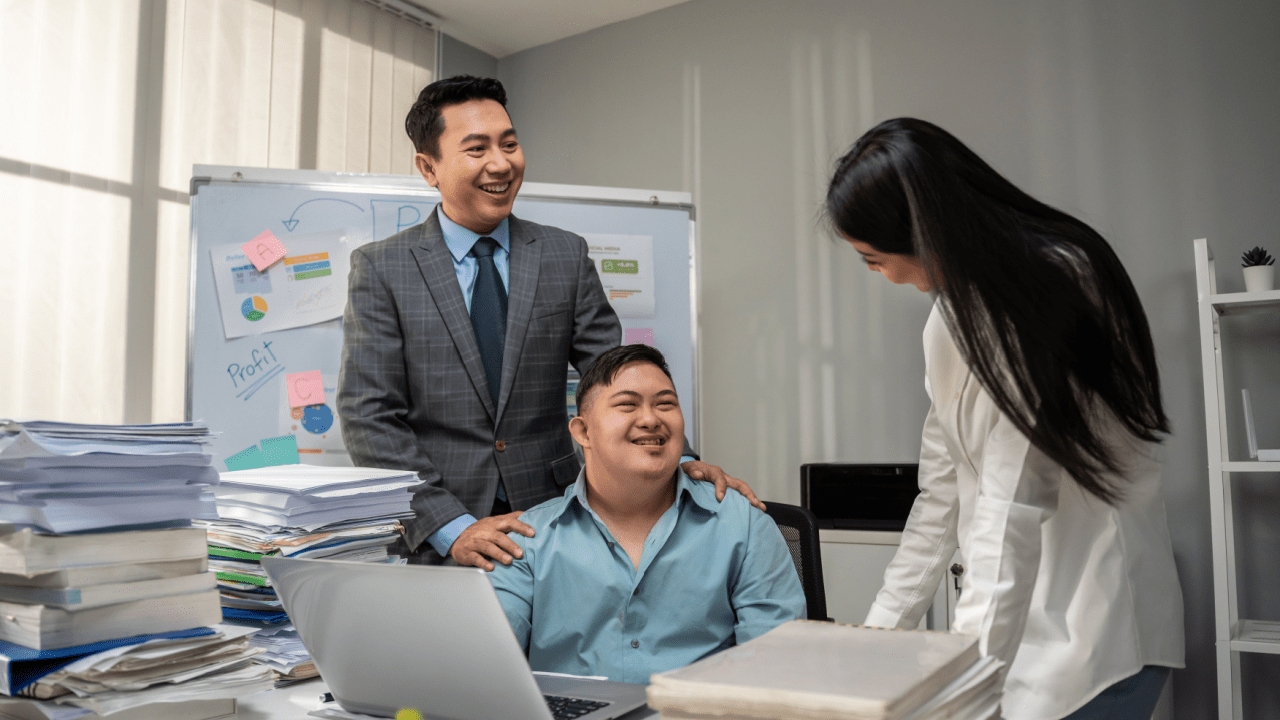 What is the 5/5 Year Rule for SSDI Three business professionals collaborating in an office - a man in a gray suit standing with his hand on the shoulder of a colleague seated at a laptop, while a woman in white stands nearby reviewing documents.