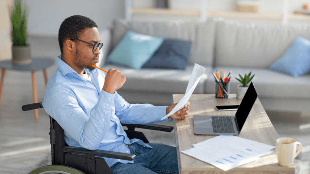 Man in wheelchair reviewing documents while researching can you collect Social Security and disability at the same time at home office desk