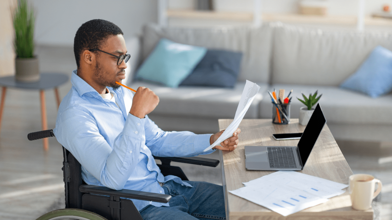 Man in wheelchair reviewing documents while researching can you collect Social Security and disability at the same time at home office desk