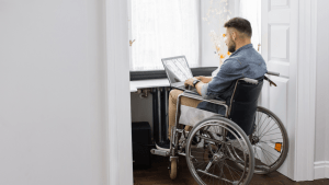 Man in wheelchair researching how long does social security disability last while working on laptop at modern office desk