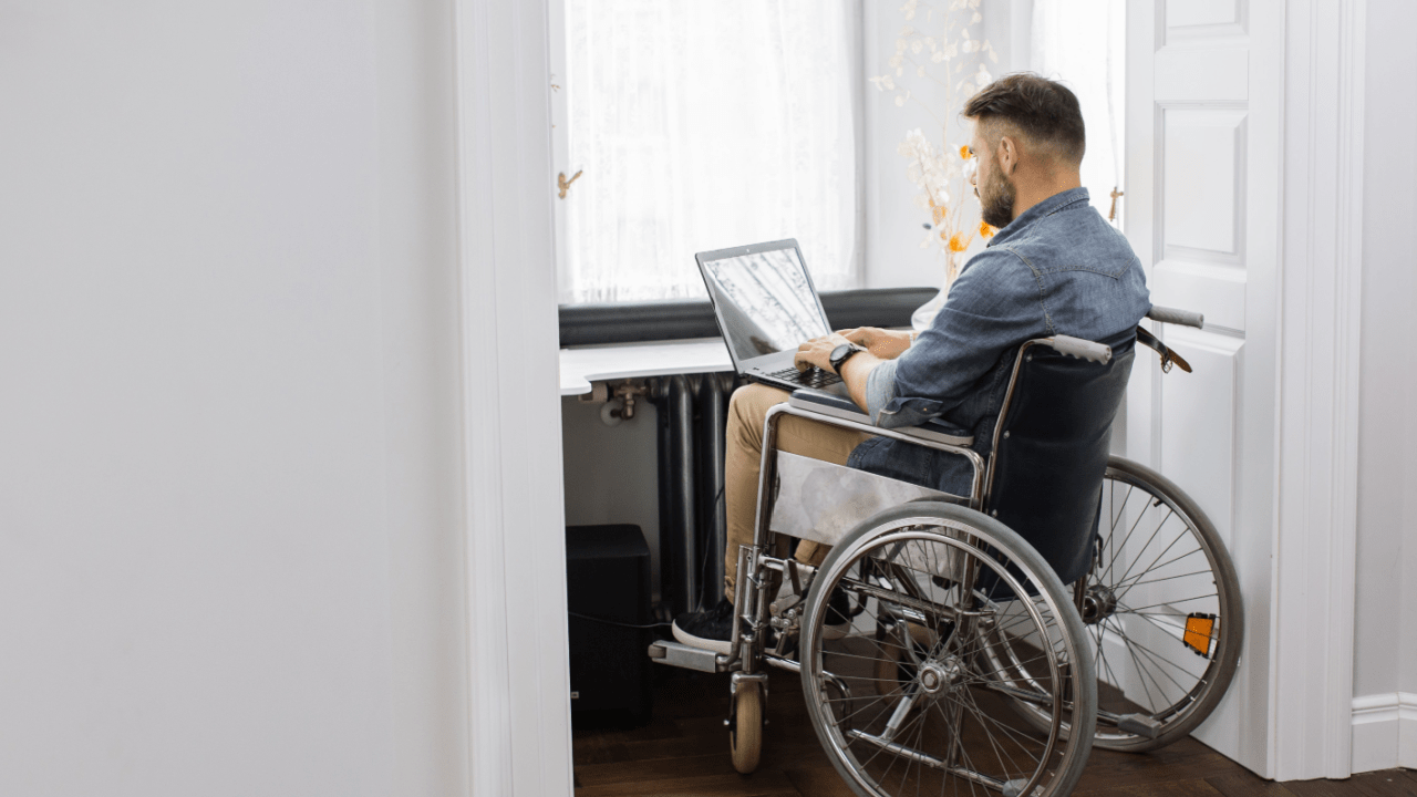 Man in wheelchair researching how much do you receive on social security disability while working on laptop at home with dog nearby