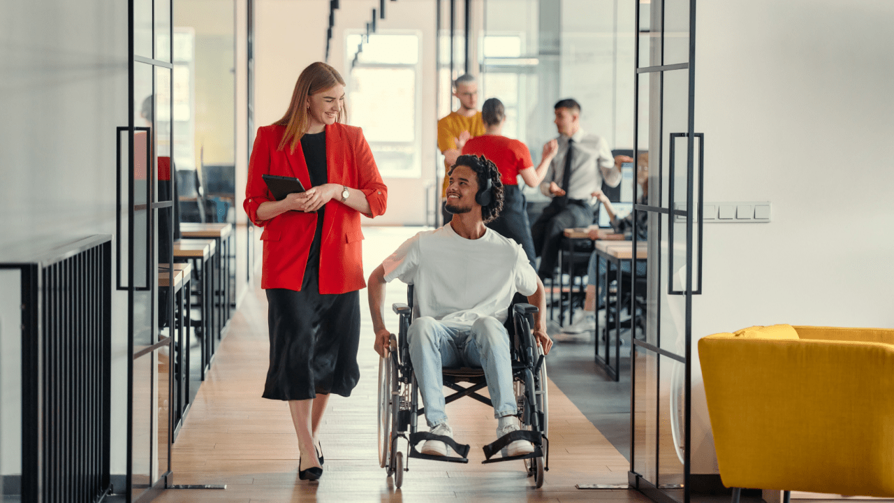 Professional woman assisting man in wheelchair discussing how much is a max out disability payment in modern office setting during disability benefits consultation