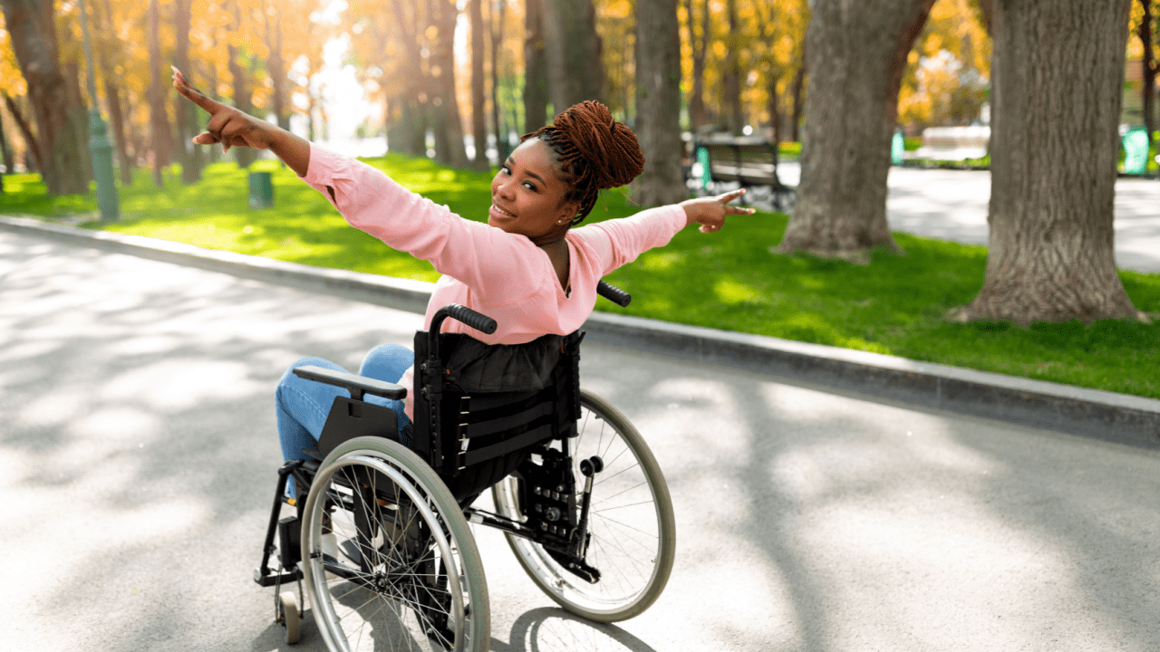 Young woman in wheelchair celebrating outdoors after learning how do they calculate how much you get for social security disability in sunny park setting