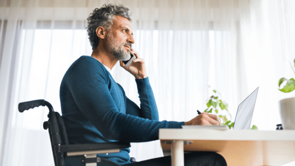 Man in wheelchair researching how much is the lowest rate of disability benefits while working at laptop in bright home office