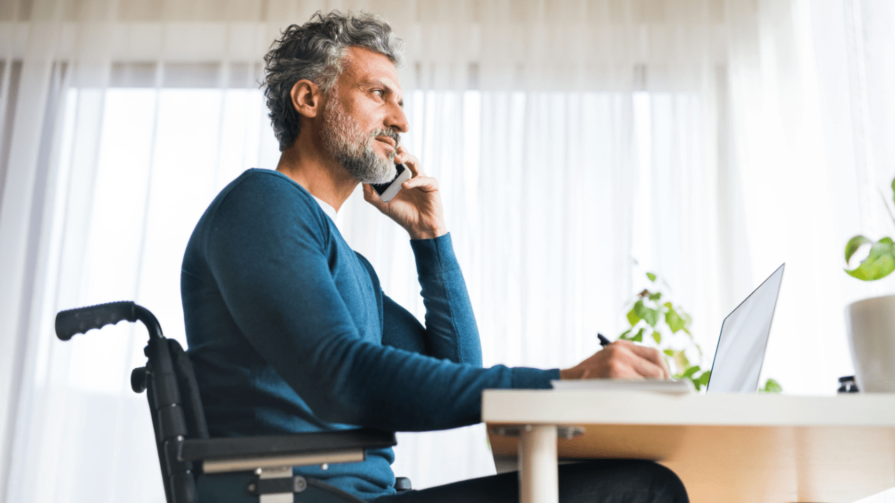 Man in wheelchair researching how much is the lowest rate of disability benefits while working at laptop in bright home office