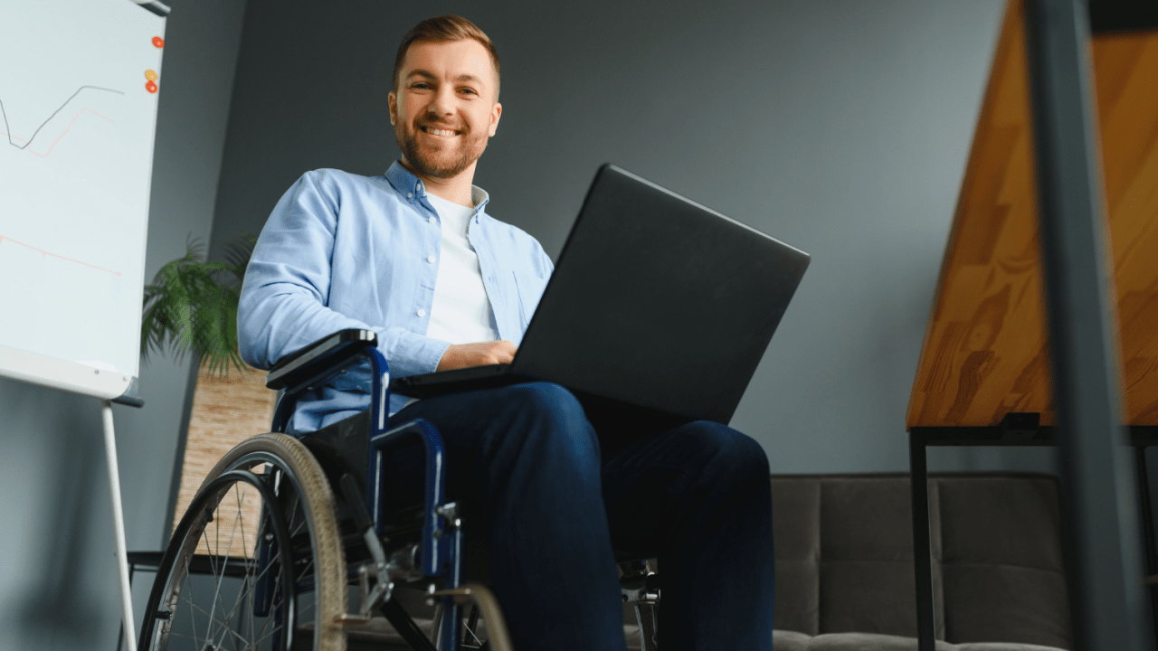 Professional man in wheelchair working on laptop in modern office, representing individuals seeking Social Security disability benefits