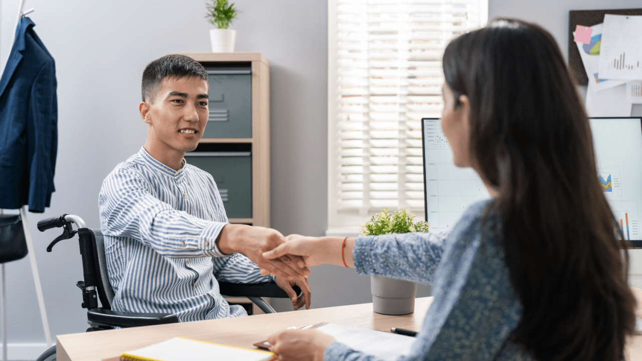 Person in wheelchair shaking hands with professional in office setting during meeting