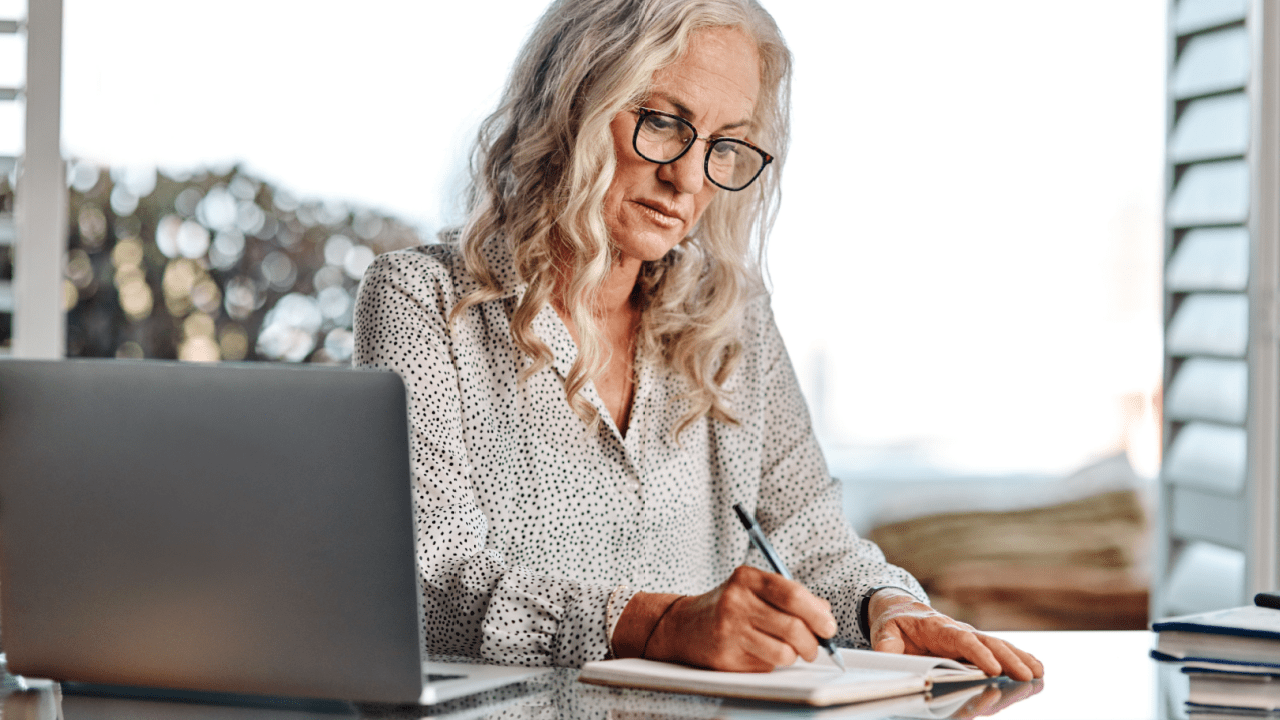 Senior woman with glasses taking notes while researching can you work while on SSDI
