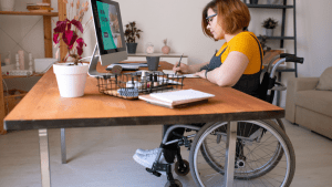 Woman in wheelchair working at computer researching what automatically qualifies you for disability benefits