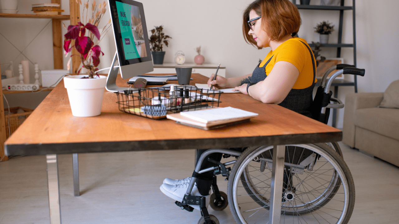 Woman in wheelchair working at computer researching what automatically qualifies you for disability benefits
