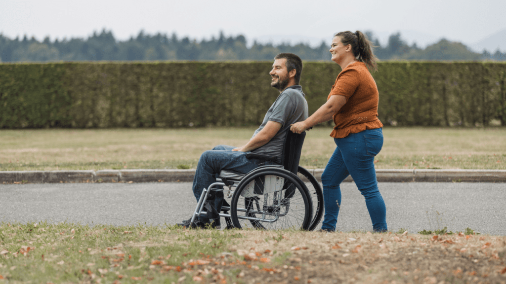 Man in wheelchair receiving assistance representing what illnesses are classed as disability