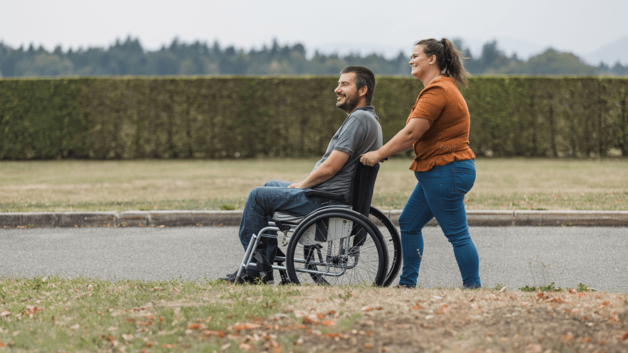 Man in wheelchair receiving assistance representing what illnesses are classed as disability