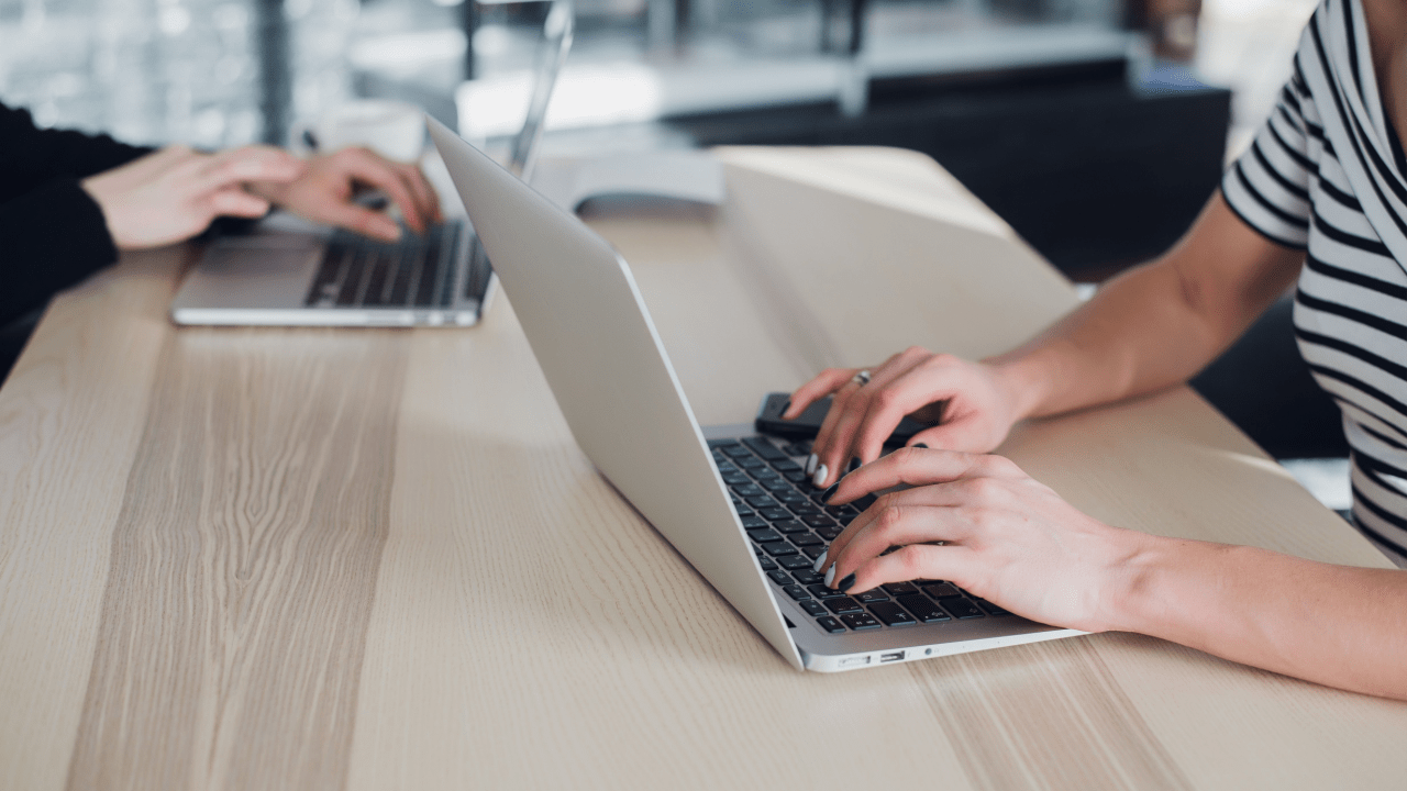 Two people working on laptops at wooden desk researching disability approval chances and legal help, comparing legal representation benefits online