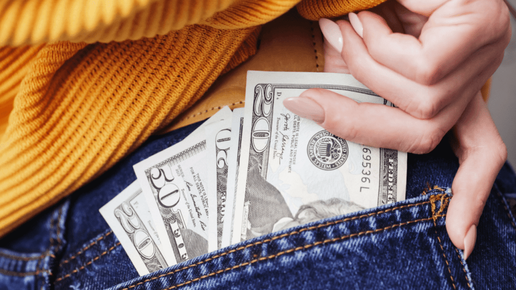 Person in yellow sweater protecting dollar bills in jeans pocket representing SSDI back pay after reconsideration approval timeline