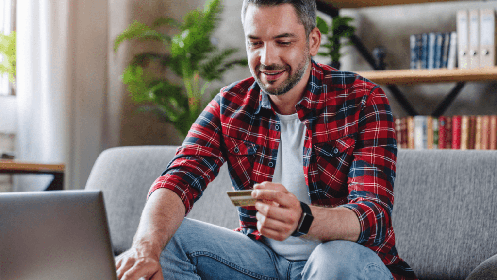 Man smiling while holding credit card and using laptop to manage finances after learning how many months does SSDI back pay cover