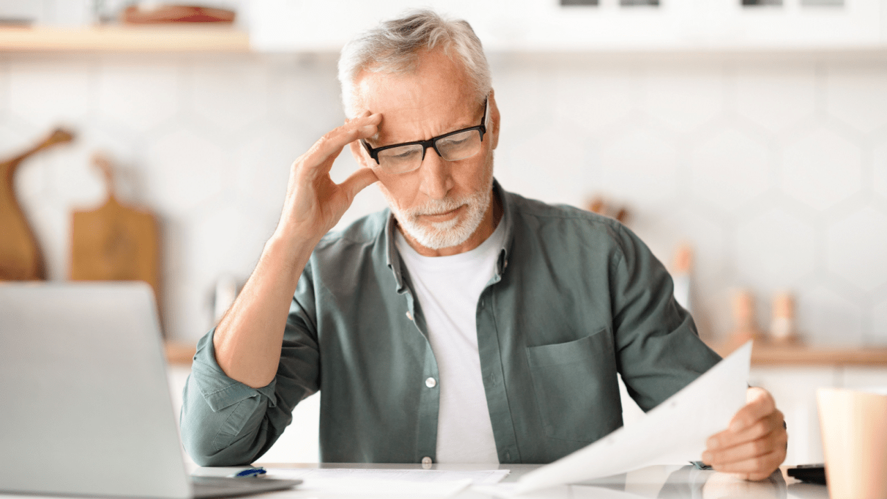 Older man with glasses holding head in frustration while reviewing SSDI reconsideration paperwork, illustrating how to guarantee SSDI approval on reconsideration stress