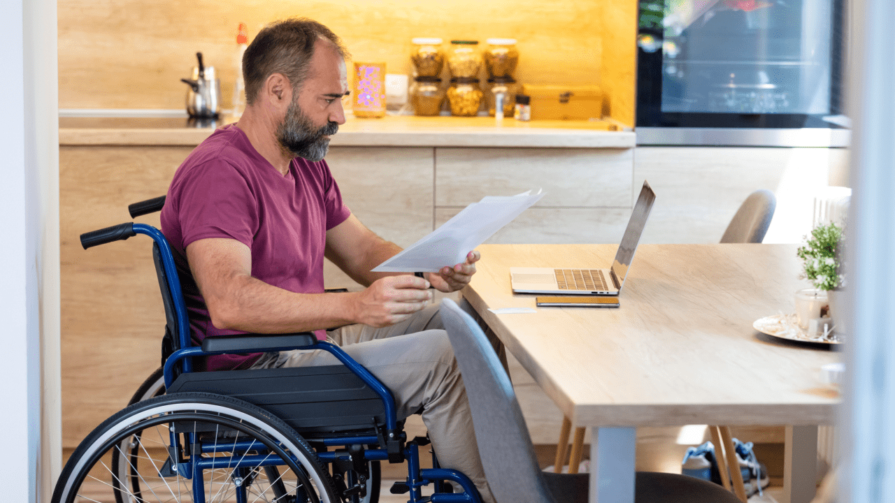 Man in wheelchair reviewing disability documents at home learning what are the three stages of disability