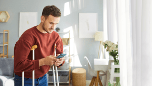 Man with mobility disability using crutches while checking phone for SSDI approval rate by stage information in modern home