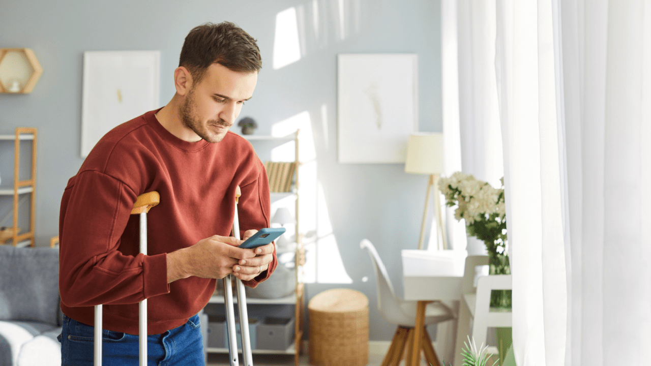 Man with mobility disability using crutches while checking phone for SSDI approval rate by stage information in modern home
