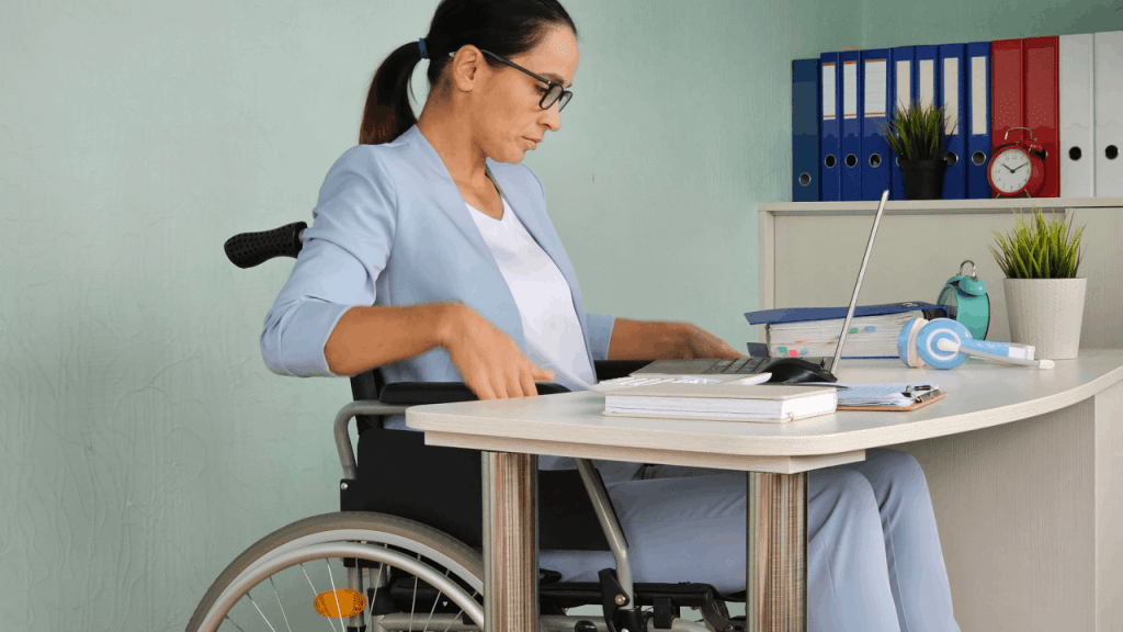 Professional woman in wheelchair learning how to apply for SSDI disability benefits while working on laptop at office desk