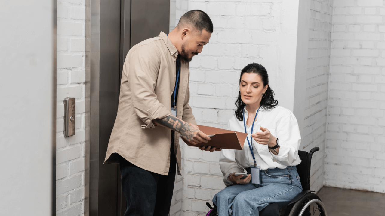 A man holding a clipboard reviews CDR documents with a woman in a wheelchair during an SSDI Continuing Disability Review consultation