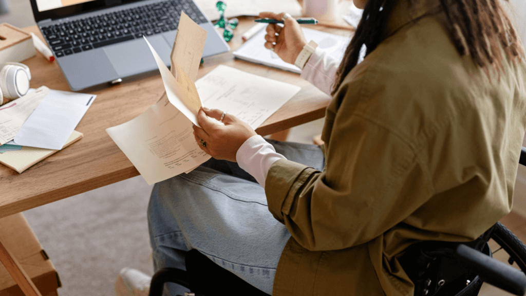 Woman in wheelchair reviewing Social Security disability review documents at a desk with a laptop