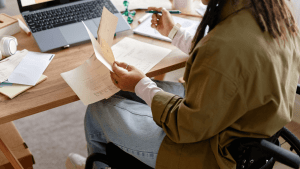 Woman in wheelchair reviewing Social Security disability review documents at a desk with a laptop